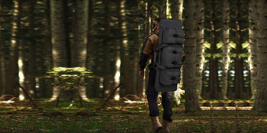 Person walking through a forest with a black rifle bag strapped to their back